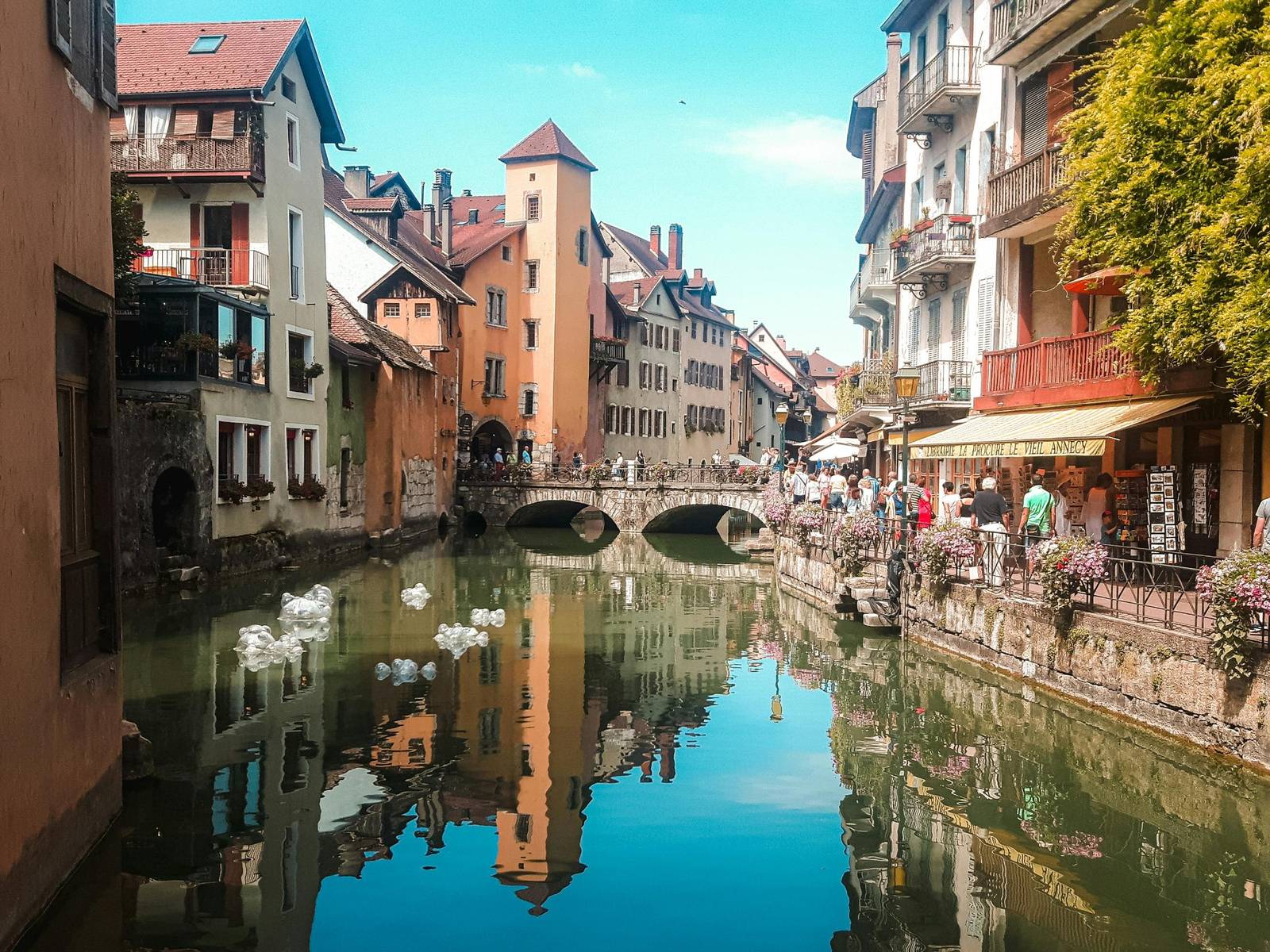 Les façades colorées de la vieille ville d’Annecy et un pont de pierre se reflètent dans le canal du Thiou, bordé de fleurs